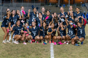 Redwood players crouch and stand together on the field for a group photo, cheering, waving and smiling.