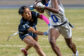 A Madera ball carrier holding the football runs upfield while a Redwood defender lunges toward her waist to grab the flag on her belt.